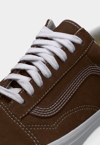 Καφέ σουέντ αθλητικό παπούτσι με λευκές ραφές, λευκά κορδόνια και λευκή λαστιχένια σόλα, που δείχνει μια κοντινή λήψη από το πλάι και από πάνω.