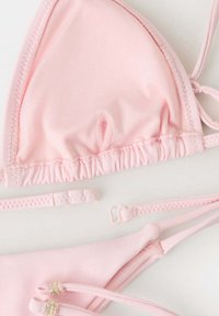 Bikini deux pièces rose clair avec bretelles réglables posé à plat sur une surface blanche.