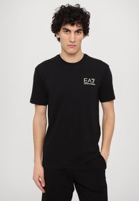 Melna crew-neck T-kreklu izgatavots no kokvilnas, ar mazu baltu EA7 logo uz krūšu daļas un teksturētām akcentiem uz pleciem.
