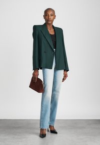 Double-breasted dark green blazer, black tank top, light-wash straight-leg jeans, brown circular handbag, and black pointed-toe heels.