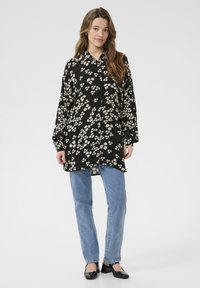 Schwarz-blaues, knopfbares Hemd mit langen Ärmeln, das kleine weiße Blumenmuster aufweist. Kombiniert mit hellblauen Jeans und schwarzen Schuhen.