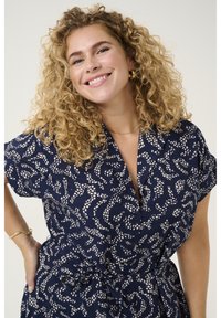 Navyblaues gemustertes Hemdkleid mit kurzen Ärmeln, lockerer Passform, Taillenknoten, mit weißen abstrakten Designs und einer Knopfleiste vorne.