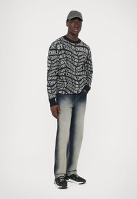 Svart och vit mönstrad tröja med texten "COUTURE", kombinerad med ljusblå denimjeans och svarta sneakers. Hatt ingår.