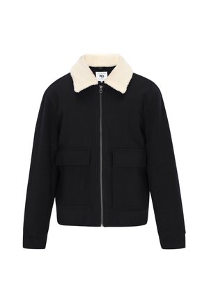 Must mustaga, millel on lukuga ees, kreemjat faux karva krae, kaks esist pocketit ja ribavarrukad. Kujundatud on see lõdva istuvuse ja sileda tekstuuriga.