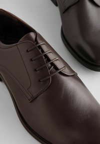 Pantofi de dress din piele maro, cu o textură netedă, design cu șireturi și vârful rotunjit. Accentuați cu detalii de cusătură pe laterale.