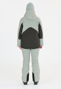 Ljusgrå skidjacka med svarta detaljer, huva och matchande byxor. Materialet verkar vattentåligt med en slät struktur och en åtsittande design.