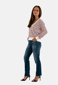 Pull rayé rouge et marine, design en v, associé à un jean bleu ajusté et des talons aiguilles noirs. Texture lisse, style décontracté.
