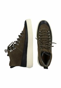 Calzature con tomaia in suede verde oliva, dettagli in pelle nera, occhielli metallici rotondi e una suola in gomma bianca a contrasto con finitura texturizzata.