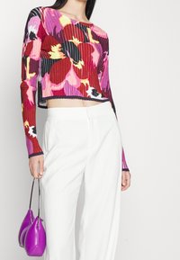 Hladký, zkrácený svetr v živých barvách (červená, růžová, žlutá a černá) s dlouhými rukávy; zkombinovaný s bílými kalhotami a fialovou taškou.