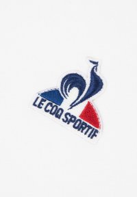 Il logo ricamato presenta sezioni blu e rosse con testo bianco che recita "LE COQ SPORTIF." Si trova su uno sfondo bianco.
