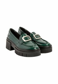 Mocasines de charol verde con gruesos tacones negros estriados y grandes hebillas rectangulares plateadas en la parte superior.