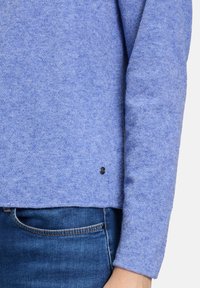 Pull bleu avec une finition texturée, détail de logo noir rond à l'ourlet et manches longues. Associé à un jean bleu foncé.