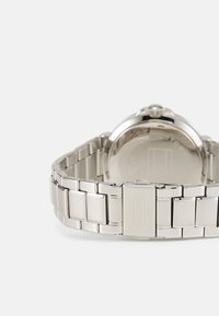 Montre en métal argenté avec une finition polie et brossée, dotée d'un boîtier rond et d'un bracelet maillé, affichant un design minimaliste.