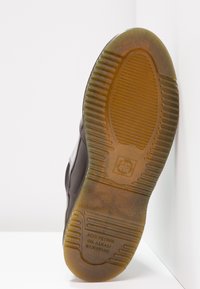 Semelle de chaussure avec un motif de bande de roulement texturé et un texte en relief indiquant "ACID PETROL OIL ALKALI RESISTANT" sur un matériau en caoutchouc ambre.