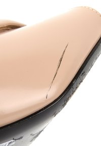 Gros plan d'une chaussure beige avec une semelle noire, montrant une rayure visible sur la surface lisse en cuir près de la zone des orteils.