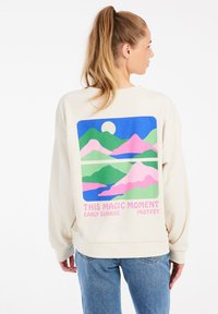Sweat-shirt couleur crème avec un graphique coloré de montagnes et d'un soleil au dos, avec le texte "CE MOMENT MAGIQUE PROTESTATION DE L'AUBE".