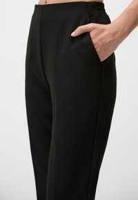 Zwarte broeken van gladde stof, met zijzakken, een aangesloten ontwerp en een elastische tailleband.