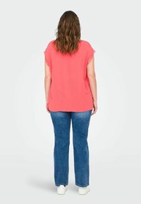 Top corto corallo a maniche corte con bordi scallop, abbinato a jeans blu a gamba dritta e sneakers bianche, visto da dietro.