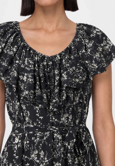 Black dress with white floral pattern, ruffled neckline, short flutter sleeves, and waist tie worn by a person with short dark hair.