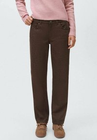 Pantalones de mezclilla marrones de corte recto con una textura sutil y bolsillos frontales, combinados con un suéter de punto rosa claro y zapatillas marrones.