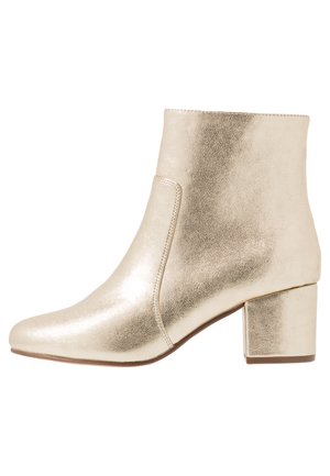 Bottines métalliques dorées avec un bout pointu, texture lisse et un talon bloc. Présente un design à enfiler sans matériel visible.