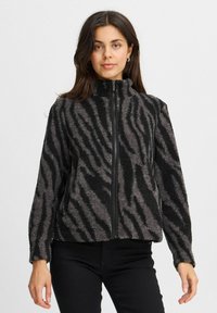 Veste en polaire noire et grise avec fermeture éclair devant, col montant et motif zébré. Présente une coupe décontractée et une surface texturée.