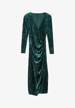 Abito di velluto verde scuro, con maniche lunghe, scollatura a V, dettagli drappeggiati sul davanti e una silhouette aderente.