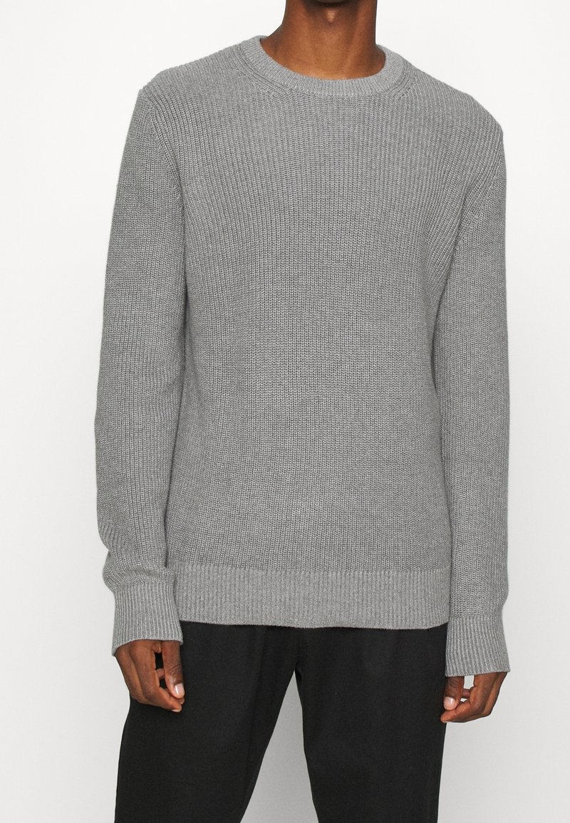 Maglione grigio lavorato a maglia con scollo rotondo, polsini e orlo a coste. Tessuto testurizzato con una vestibilità morbida, mostrato abbinato a pantaloni neri.