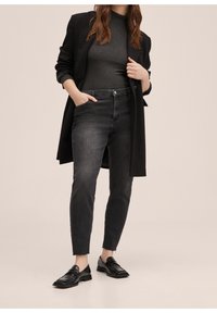 Blazer noir porté sur un haut gris ajusté, associé à un jean noir taille haute avec un ourlet effiloché et des mocassins noirs. Design simple et épuré.