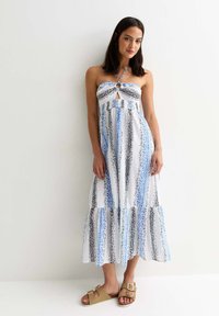 Strapless maxiklänning i vitt, med blå och svarta prickiga ränder, en nyckelhålsdetalj och en volangslutning. Matchad med sandaler i tan.