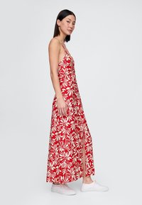 Rød maxikjole med blomsterprint og hvide bladmønstre, tynde stropper og sideslids. Brugt med hvide sneakers, med en tætsiddende overdel.