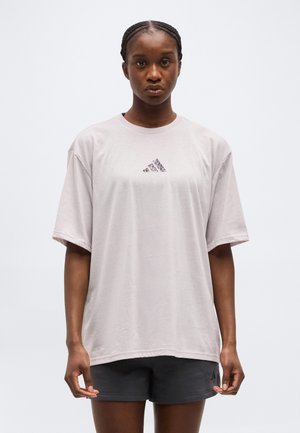 Woman with braided hair wearing an oversized light gray Adidas t-shirt and black shorts against a plain white background.