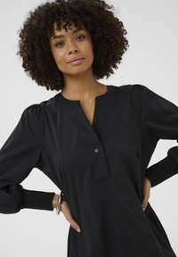 Fekete gombos ruha, galléros nyakkal, puffos ujjakkal, textúrált mandzsettákkal és laza szabással. Könnyű anyagból készült.