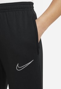 Schwarze Nike-Jogginghosen mit einer glatten Textur, elastischem Bund, Seitentasche und einem reflektierenden grauen Logo am linken Oberschenkel.