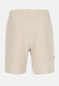 Shorts en tissu beige au design texturé, avec une taille élastique et un ourlet droit, comportant une étiquette latérale visible.