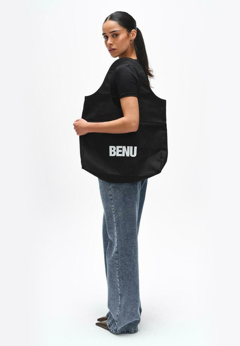 Czarna torba na ramię z napisem "BENU" w kolorze białym, charakteryzująca się solidną konstrukcją i szerokimi ramiączkami, zestawiona z niebieskimi dżinsami.
