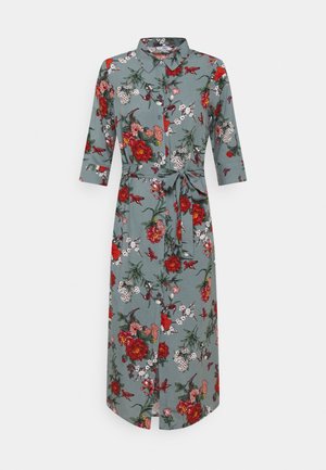 Robe midi boutonnée verte avec imprimé floral rouge et blanc, manches trois-quarts, col et ceinture en tissu nouée à la taille.