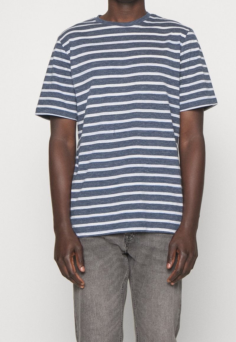 Modrá a bílá pruhovaná tričko s krátkým rukávem, kulatý výstřih, vyrobené z měkkého materiálu. V kombinaci se šedými džíny. Viditelné švy.