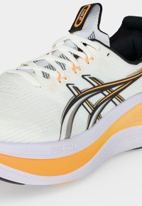 Λευκό και πορτοκαλί παπούτσι τρεξίματος Asics με μαύρο λογότυπο, λευκά κορδόνια, επενδεδυμένη σόλα και μαύρο επενδυμένο εσωτερικό.