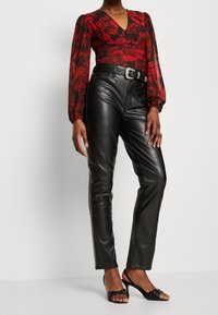 Pantalons en cuir noir taille haute au design ajusté avec fermeture éclair, associés à un blouse à manches longues à motif floral rouge.