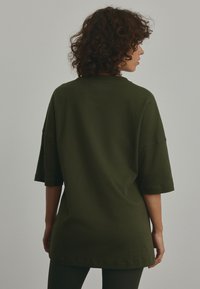Oversized dark green t-shirt made of smooth cotton fabric, featuring short sleeves, a crew neck, and a plain back without embellishments.