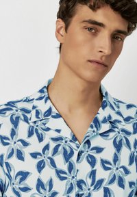 Kurzarm-Hemd aus hellblauem Stoff mit einem dunkelblauen Blumenmuster, ausgestattet mit einem eingeschnittenen Kragen und Knopfverschluss. Strukturierter Entwurf.