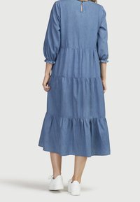 Blå denimklänning med ett lagerdesign, puffärmar och en nyckelhålsrygg. Avslutad med en volangkant i ankellängd och bärs med vita sneakers.