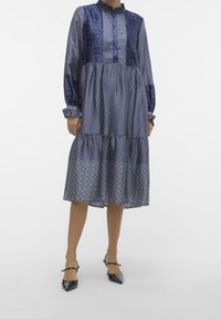 Abito blu navy con chiusura a bottoni, caratterizzato da un mix di motivi geometrici e trame, maniche lunghe e gonna a balze.