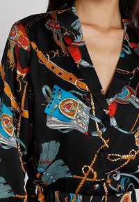 Camicia nera in satin con colletto, caratterizzata da un motivo a tema equino colorato in rosso, blu e bianco. Accenti notevoli includono hardware dorato.