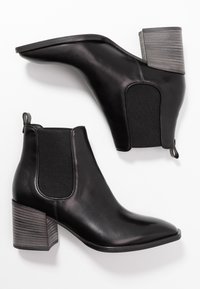 Stivali alla caviglia in pelle nera con punta affusolata, pannelli laterali elasticizzati e tacco a blocco testurizzato. Superficie liscia con finitura opaca.