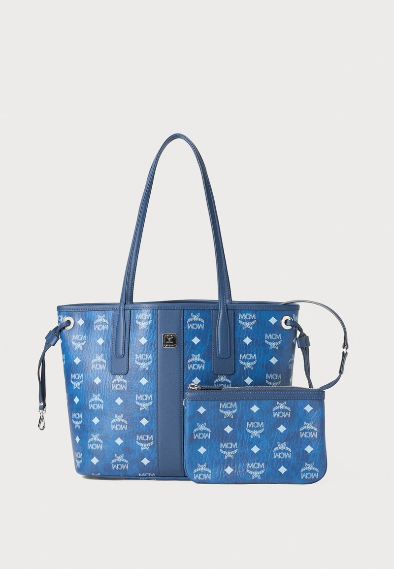 Niebieska torba tote z podwójnymi uchwytami, ozdobiona wytłoczonymi logo MCM oraz wzorem diamentów; zawiera odpinaną dopasowaną saszetkę. Gładka faktura.