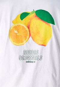 T-shirt bianca con una grafica colorata di limone, foglie verdi e una fetta d'arancia, accompagnata dal testo "ADIDAS ORIGINALS" in verde.