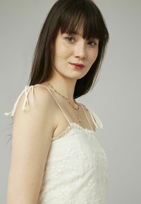 Robe sans manches blanche avec un design floral brodé, encolure volantée et bretelles ajustables. Texture lisse, tissu léger.