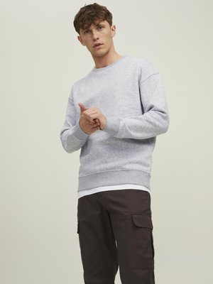 Grå sweatshirt med lange ærmer og ribbede manchetter, parret med mørke cargo bukser. Stoffet ser blødt ud, med en afslappet pasform og minimalistisk design.